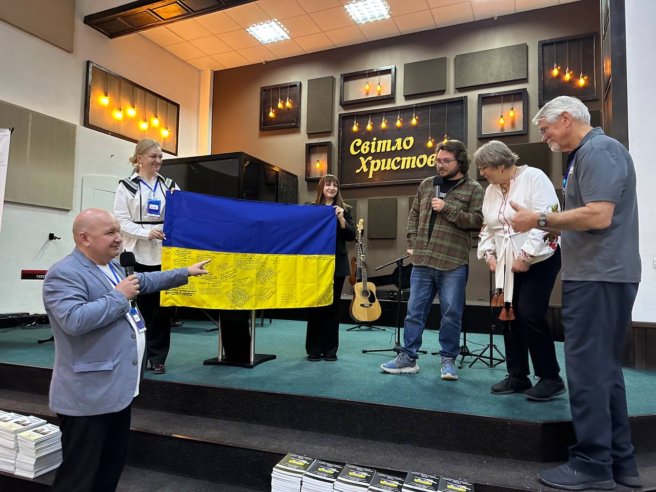 A Ukrainian flag covered with messages is held at a ministry gathering as Chris and Rahnella stand nearby.