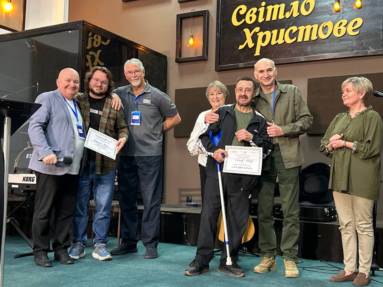 Chris and Rahnella with Ukrainian participants holding certificates on stage.